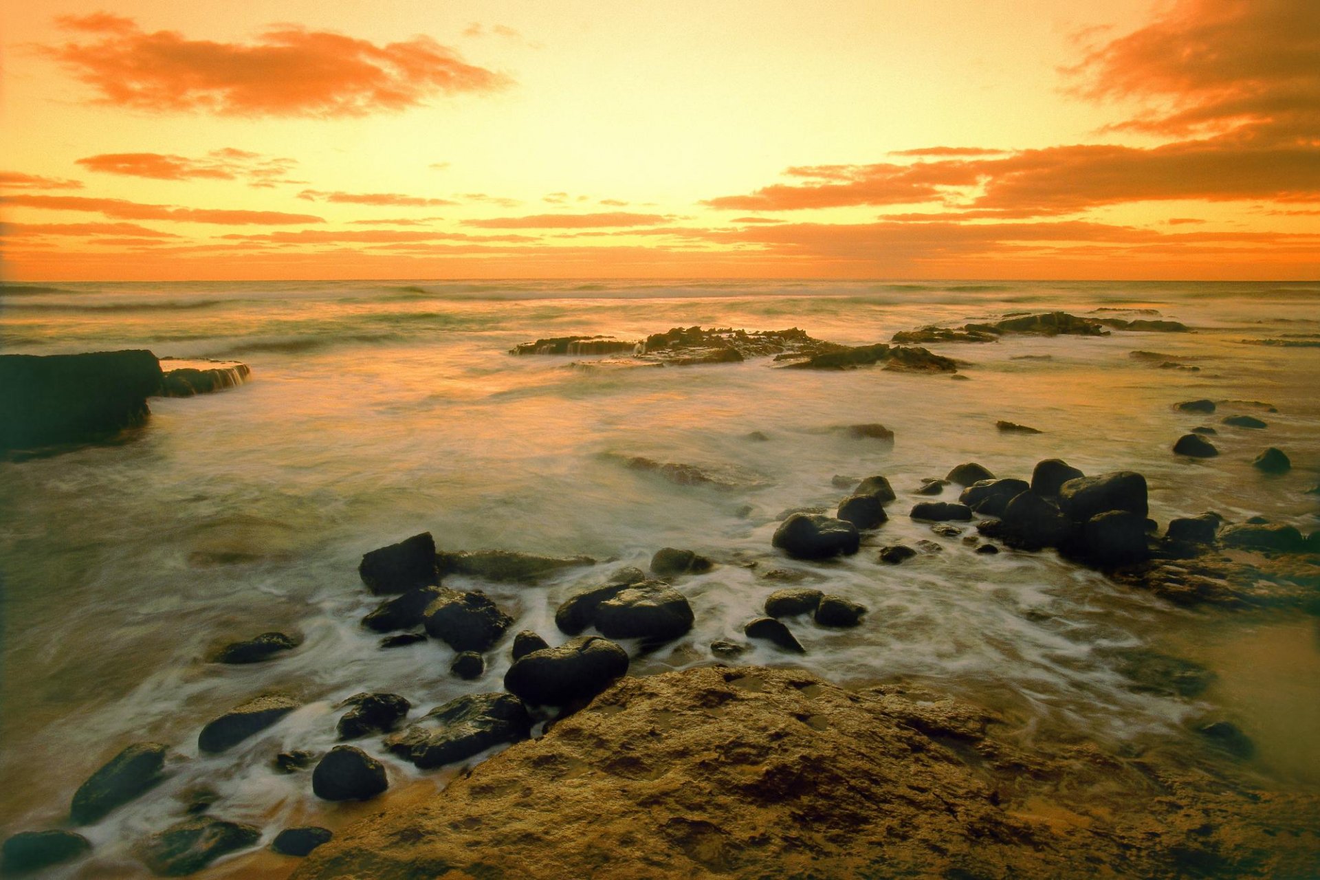 HD PC desktop wallpaper of a serene ocean scene at sunset with rocky shorelines under a glowing golden sky, showcasing nature's tranquil beauty.