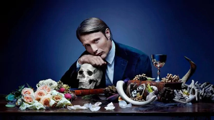 HD PC desktop wallpaper inspired by the TV show Hannibal: a suited man rests his chin on a skull amid roses, wine, horns and bone fragments on a dark dining table.