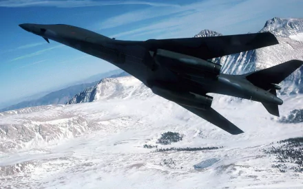 Rockwell B-1 Lancer military bomber flying over snow-covered mountains, captured in high-definition for a striking PC desktop wallpaper.