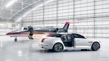 White Jaguar XJ Ultimate with rear-hinged door open beside a private jet in a glossy hangar — HD PC desktop wallpaper and background.