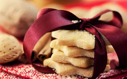 HD PC desktop wallpaper featuring a stack of star-shaped cookies tied with a burgundy ribbon, surrounded by cinnamon sticks and whole almonds on a festive cloth.