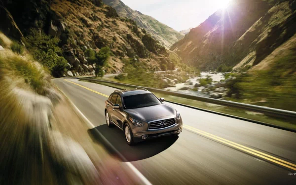 HD PC desktop wallpaper featuring an Infiniti QX70 driving on a scenic mountain road with sunlight illuminating the landscape.