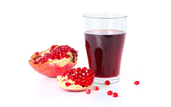 HD PC desktop wallpaper featuring a glass of deep red pomegranate juice alongside fresh pomegranate seeds and a split fruit on a white background.