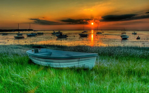 HD desktop wallpaper featuring a serene sunset over a beach with multiple boats and a prominent boat in the foreground, set against a vibrant sky and grassy area.