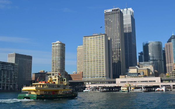 View of Circular Quay in Sydney, Australia, featuring skyscrapers, city buildings, a busy wharf, ferries, and boats in the harbor under a clear blue sky.
