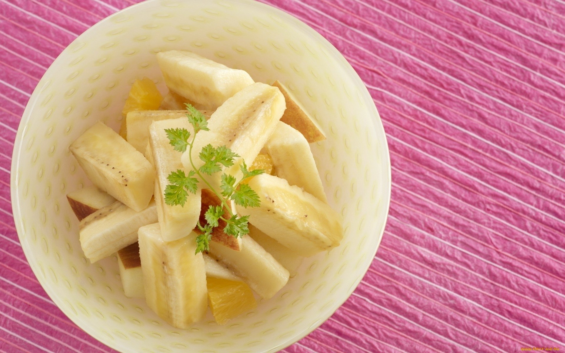 HD PC desktop wallpaper featuring a bowl of sliced bananas garnished with herbs on a textured pink surface, highlighting fresh fruit and food themes.