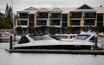 HD PC desktop wallpaper/background: a motorboat (vehicle) moored in a Brisbane marina, with waterfront apartment buildings reflected on calm sea water.