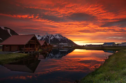 A stunning sunset over Iceland reflects vivid colors on a serene lake, framed by charming cabins and majestic mountains, making for an inspiring HD desktop wallpaper.