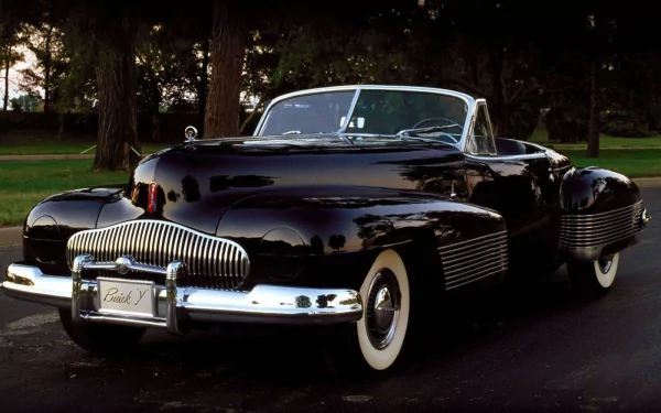 Sleek black Buick Y-Job convertible parked on a tree-lined road, high-gloss finish and chrome details — HD PC desktop wallpaper/background.