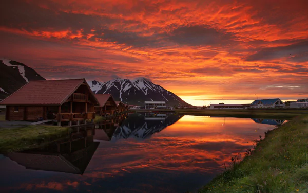 A stunning sunset over Iceland reflects vivid colors on a serene lake, framed by charming cabins and majestic mountains, making for an inspiring HD desktop wallpaper.