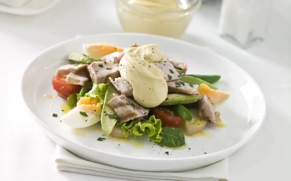 A vibrant salad featuring a mix of fresh vegetables, sliced meat, and a dollop of creamy dressing, set on a sleek white plate, serves as an inviting HD desktop wallpaper.