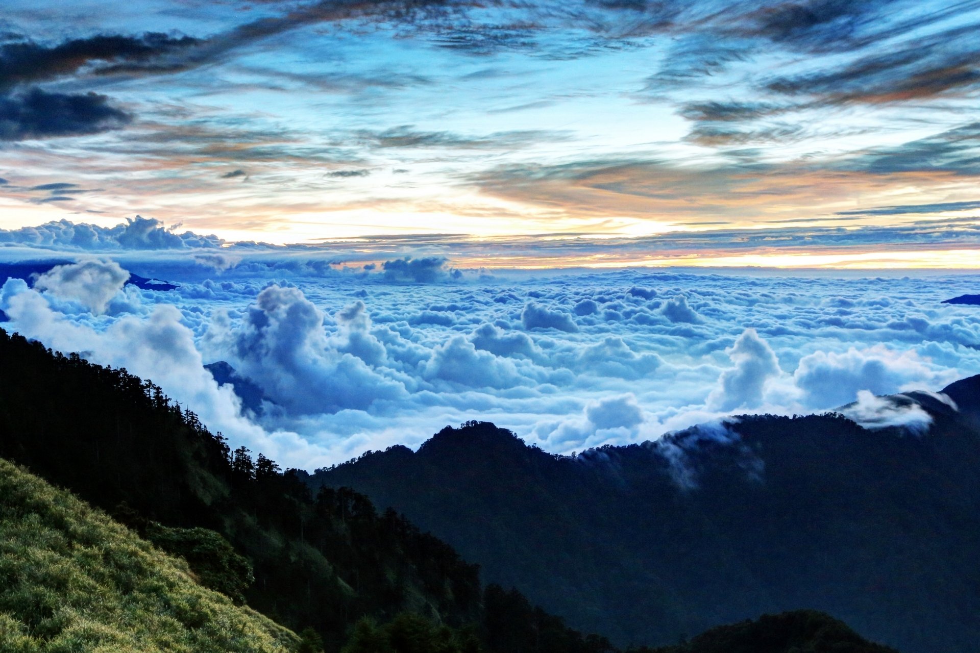 HD desktop wallpaper showing a breathtaking sea of clouds above mountain peaks under a vibrant sky, capturing the serene beauty of nature.