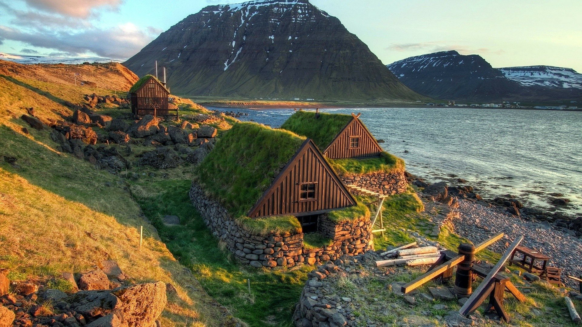 A serene view of traditional grass-roofed houses by a lake, set against a backdrop of majestic mountains, capturing the beauty of nature in high-definition photography.