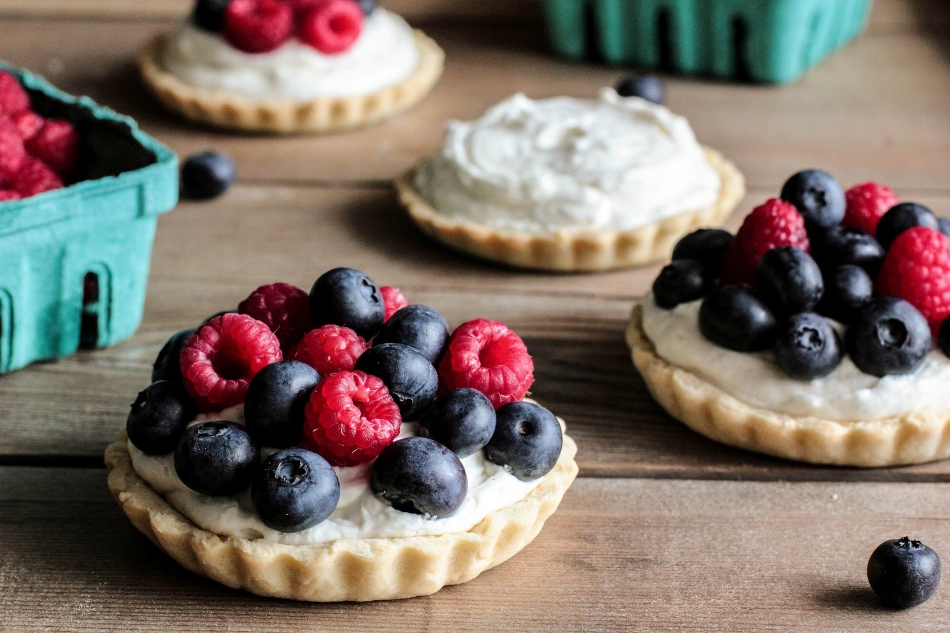HD PC desktop wallpaper featuring close-up of fruit-topped sweet tartlets with raspberries and blueberries on a wooden surface.