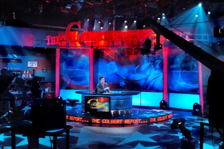HD wallpaper of The Colbert Report set featuring the host at his desk with vibrant blue and red stage lighting.