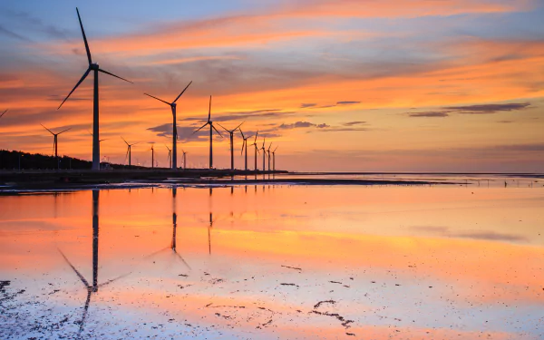 HD desktop wallpaper of man-made wind turbines lined along a reflective shoreline under a colorful sunset sky.