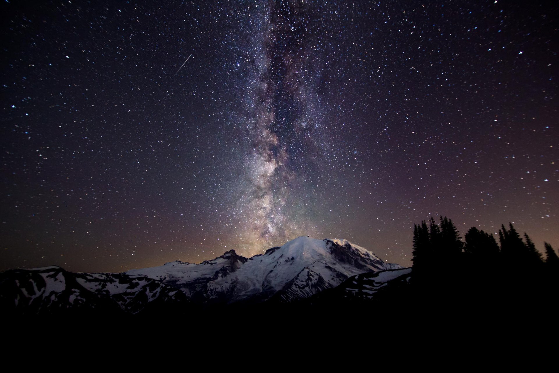 HD Sci-Fi desktop wallpaper featuring a star-filled night sky with the Milky Way stretching above a snow-capped mountain and silhouetted trees.