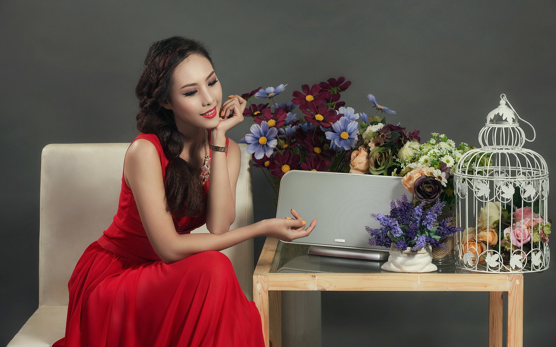 Asian woman in a red dress seated by a table with a laptop, flowers, and a decorative birdcage, captured in an HD PC desktop wallpaper and background.