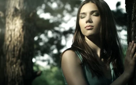 HD desktop wallpaper featuring a woman with closed eyes, leaning against a tree, exuding a tranquil and reflective mood in a forest setting.
