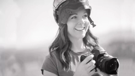 A black and white HD wallpaper featuring a smiling woman in a helmet, holding a camera, capturing the essence of music and creativity, inspired by Lindsey Stirling.
