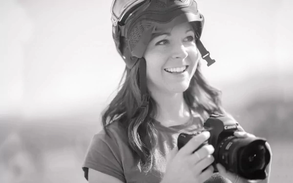 A black and white HD wallpaper featuring a smiling woman in a helmet, holding a camera, capturing the essence of music and creativity, inspired by Lindsey Stirling.