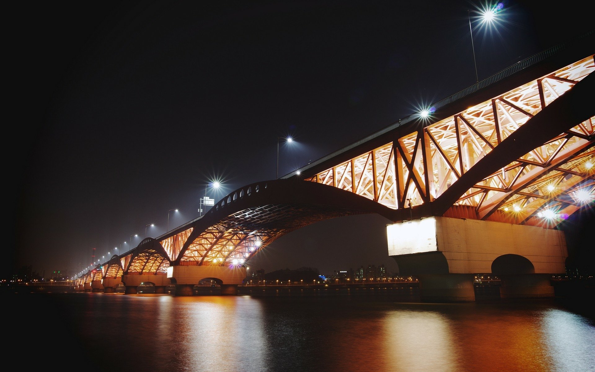 Night view of the illuminated Seongsan Bridge in Seoul, South Korea, showcasing its man-made architectural design reflected on the calm water below.