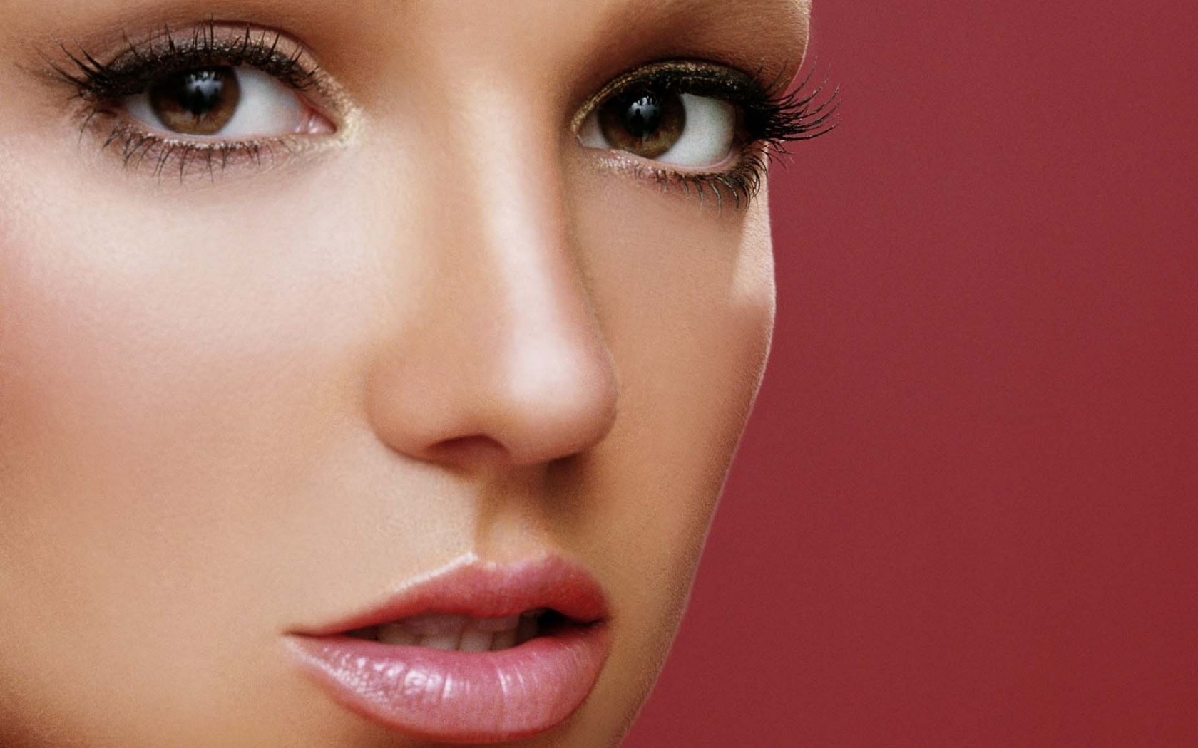 High-definition PC desktop wallpaper featuring a close-up of Britney Spears, showcasing her striking features against a rich red background.