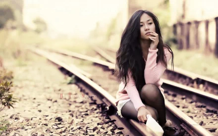 HD desktop wallpaper featuring a contemplative woman sitting on railroad tracks, surrounded by soft, natural tones.