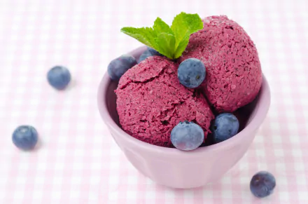 A charming HD wallpaper featuring a bowl of purple ice cream garnished with mint leaves and surrounded by fresh blueberries, set against a pastel checkered background.