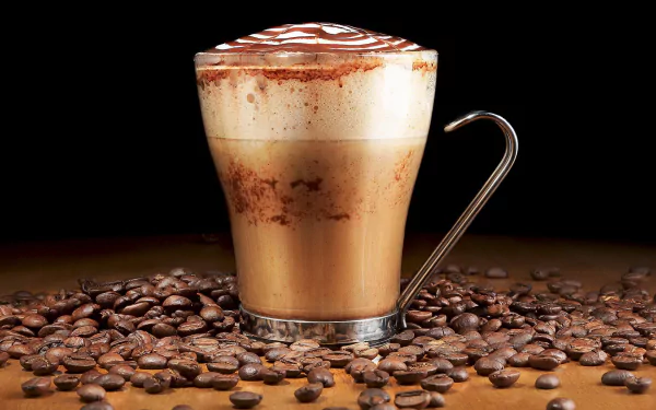 A steaming cup of coffee topped with foam and chocolate drizzle, surrounded by coffee beans, serves as a rich and inviting HD desktop wallpaper.