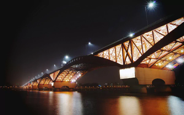 Night view of the illuminated Seongsan Bridge in Seoul, South Korea, showcasing its man-made architectural design reflected on the calm water below.
