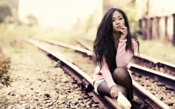 HD desktop wallpaper featuring a contemplative woman sitting on railroad tracks, surrounded by soft, natural tones.