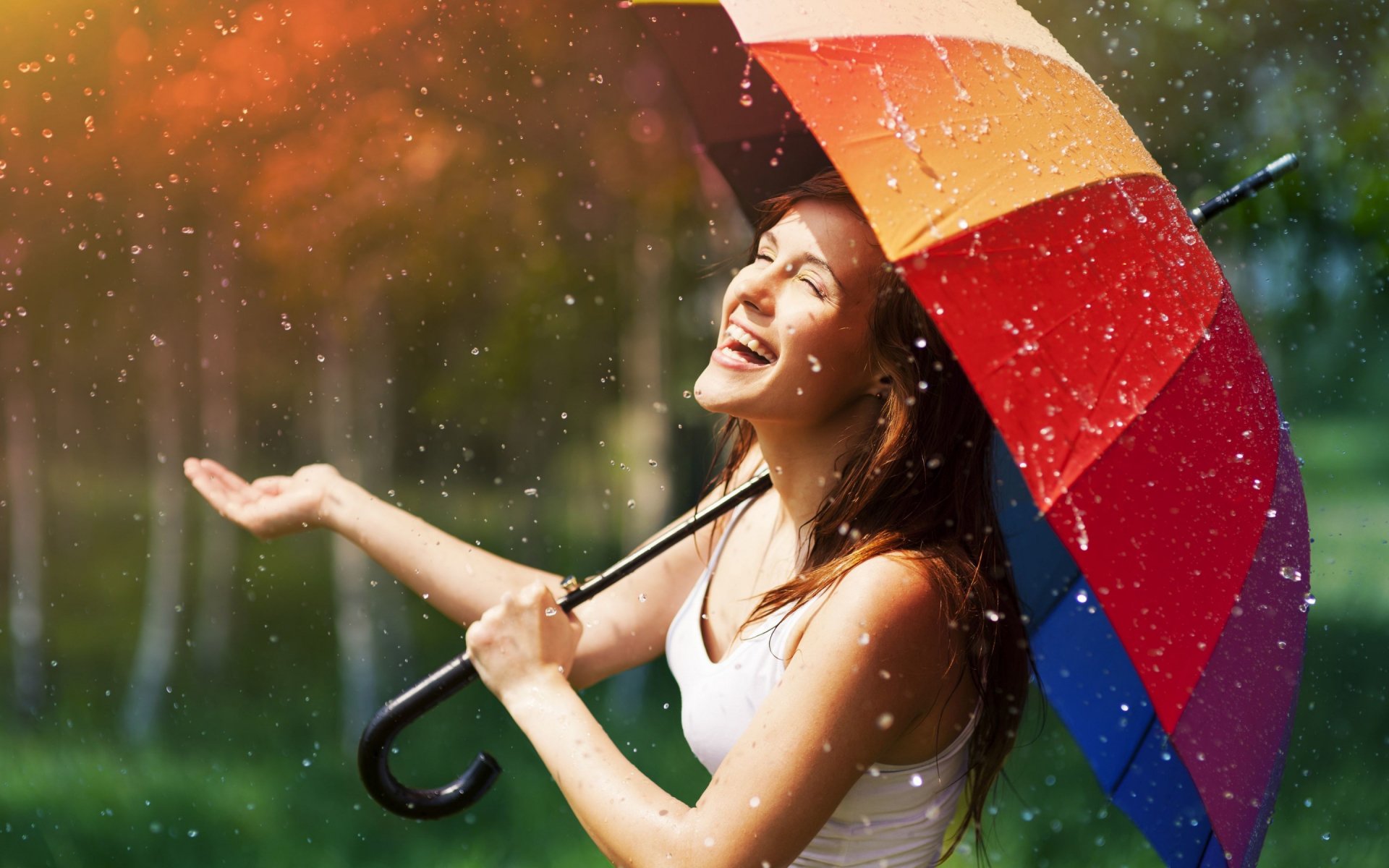 HD photography wallpaper of a joyful woman holding a colorful umbrella, enjoying raindrops with a blurred natural background, designed for PC desktop display.