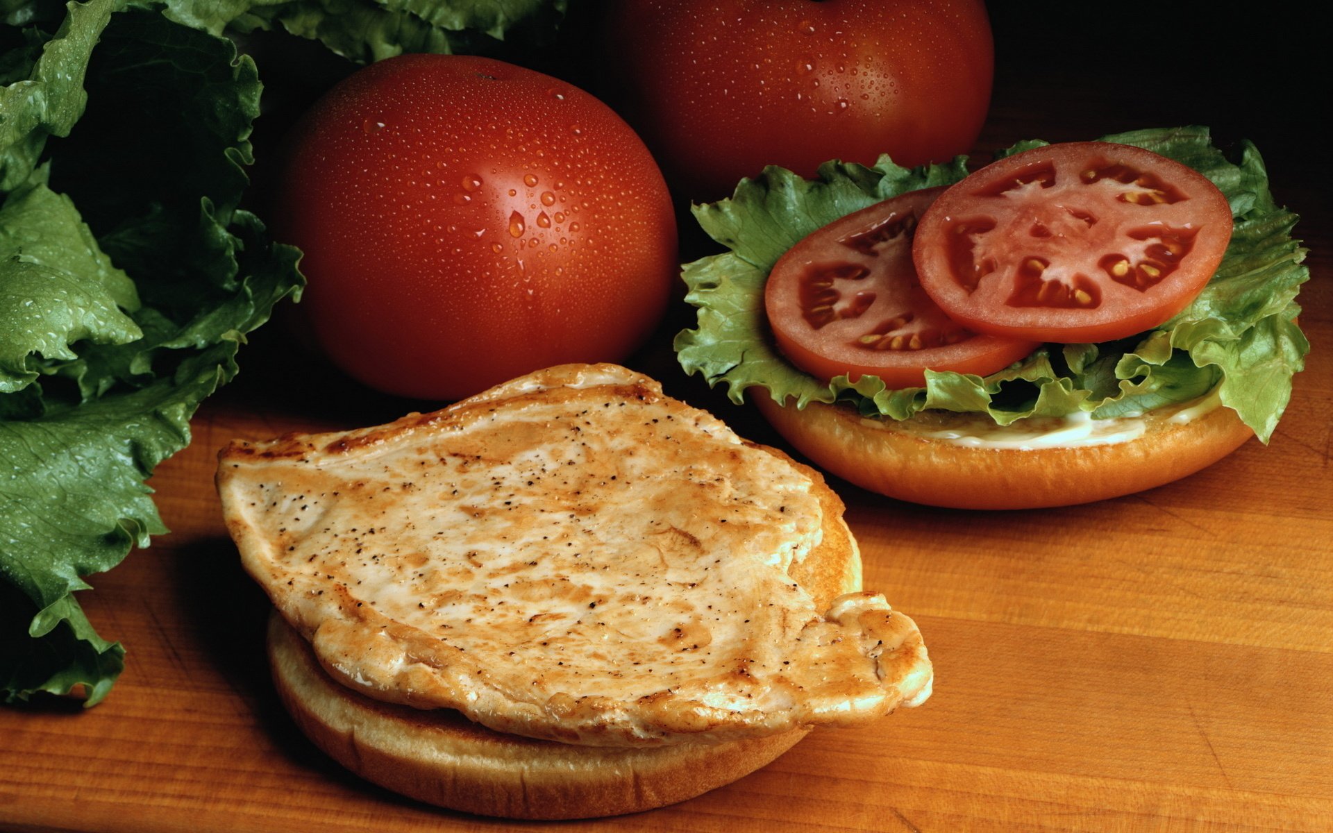 HD PC desktop wallpaper featuring a fresh chicken sandwich with lettuce, tomato slices, and whole tomatoes in the background, highlighting vibrant food colors.