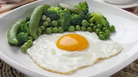 A vibrant HD desktop wallpaper featuring a perfectly cooked egg on a bed of fresh green vegetables, including broccoli, peas, and snap peas, showcasing a healthy food aesthetic.
