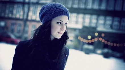 A serene Lena Meyer-Landrut gazes thoughtfully outdoors in a winter setting, wearing a cozy beanie. This HD wallpaper captures a moment in a picturesque, snowy environment.