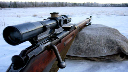 HD PC desktop wallpaper/background: man-made rifle with scope on a sandbag in a snowy field, barrel pointing toward a distant tree line.