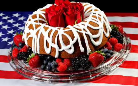 A delicious cake drizzled with white icing, adorned with strawberries, blueberries, and raspberries, crowned with vibrant red roses, set against an American flag background. HD desktop wallpaper and background.
