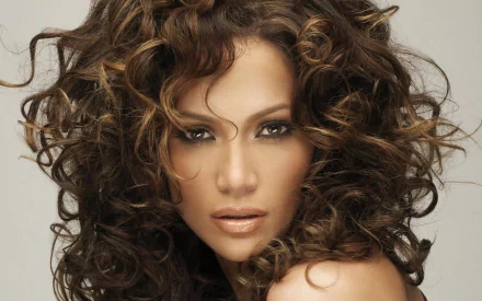 A stunning HD wallpaper featuring Jennifer Lopez, showcasing her signature curly hair and captivating expression against a soft background.