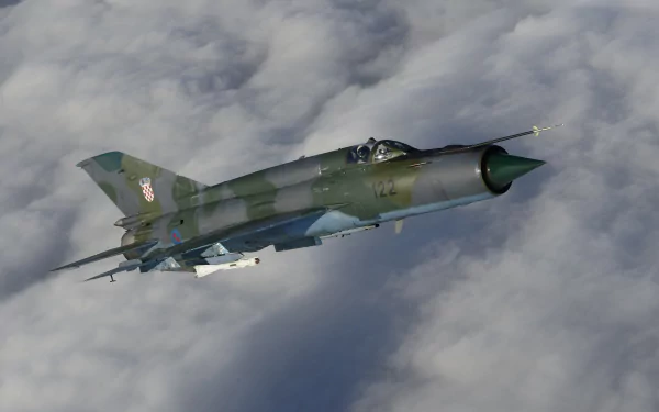 A Mikoyan-Gurevich MiG-21 fighter jet flies above the clouds, showcasing its sleek design and military markings in high-definition detail.