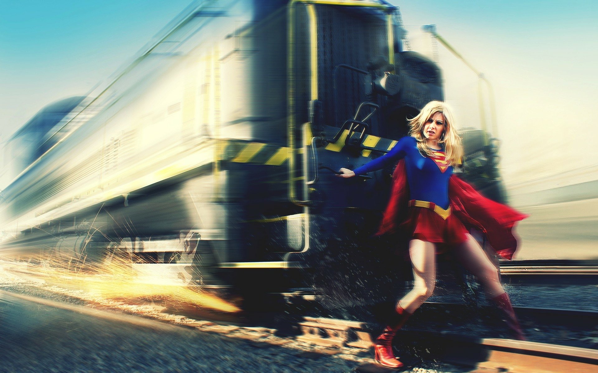 HD PC desktop wallpaper featuring a dynamic comic-style Supergirl standing confidently on train tracks with a speeding train in the background.