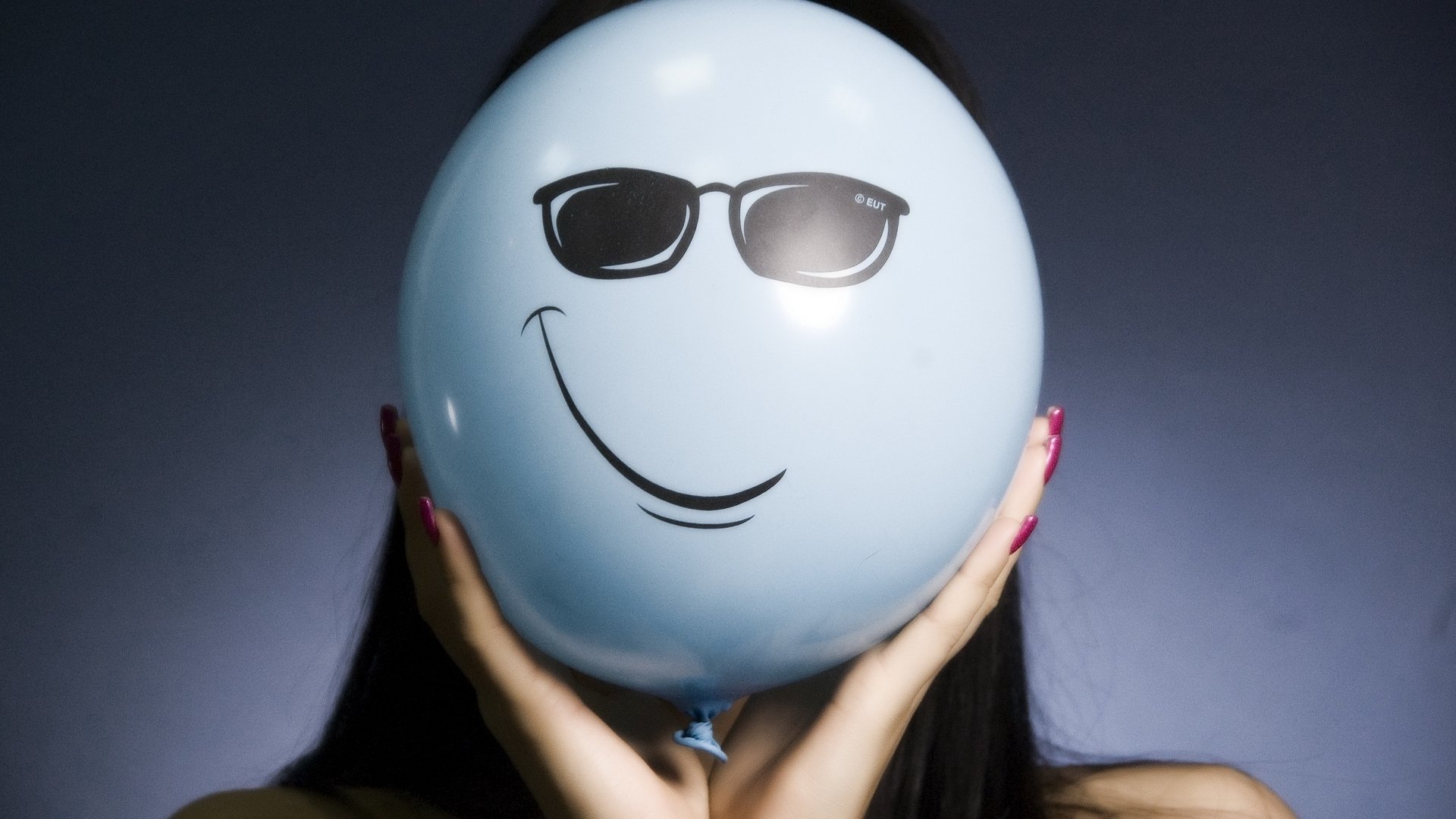 HD PC desktop wallpaper featuring a funny smiley face with sunglasses drawn on a light blue balloon held in front of a dark background.