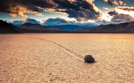 HD PC desktop wallpaper showcasing a vast desert landscape with a solitary rock leaving a trail on cracked dry earth beneath dramatic, cloud-filled skies.