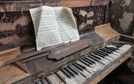 A vintage piano with worn keys and sheet music displayed on top, set against a rustic background, captures a nostalgic moment in this HD desktop wallpaper.