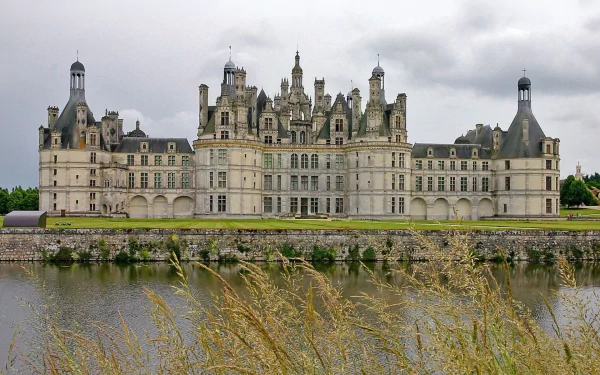 HD desktop wallpaper capturing the grand Château de Chambord, a stunning man-made Renaissance castle reflected in the calm river under a cloudy sky.