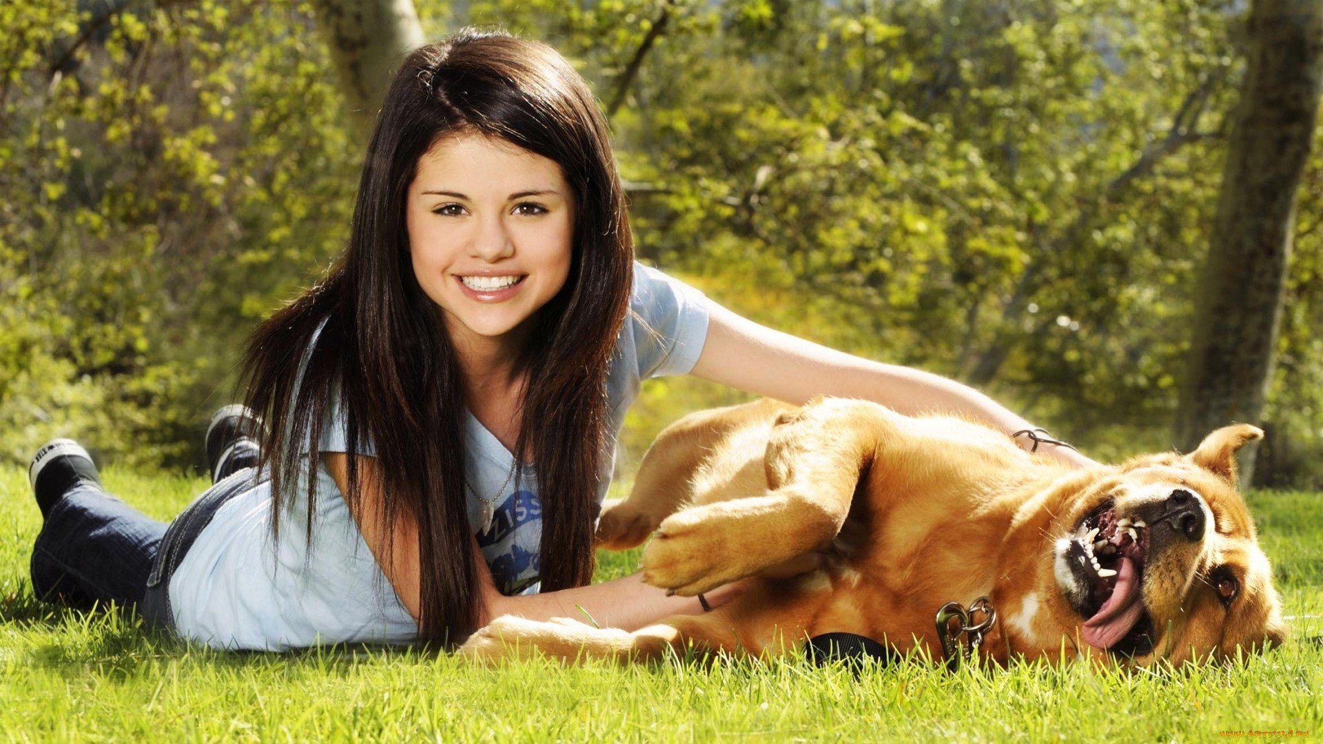 Selena Gomez smiles joyfully while lying in the grass next to a playful dog. This vibrant image makes a great HD desktop wallpaper and background for music fans.