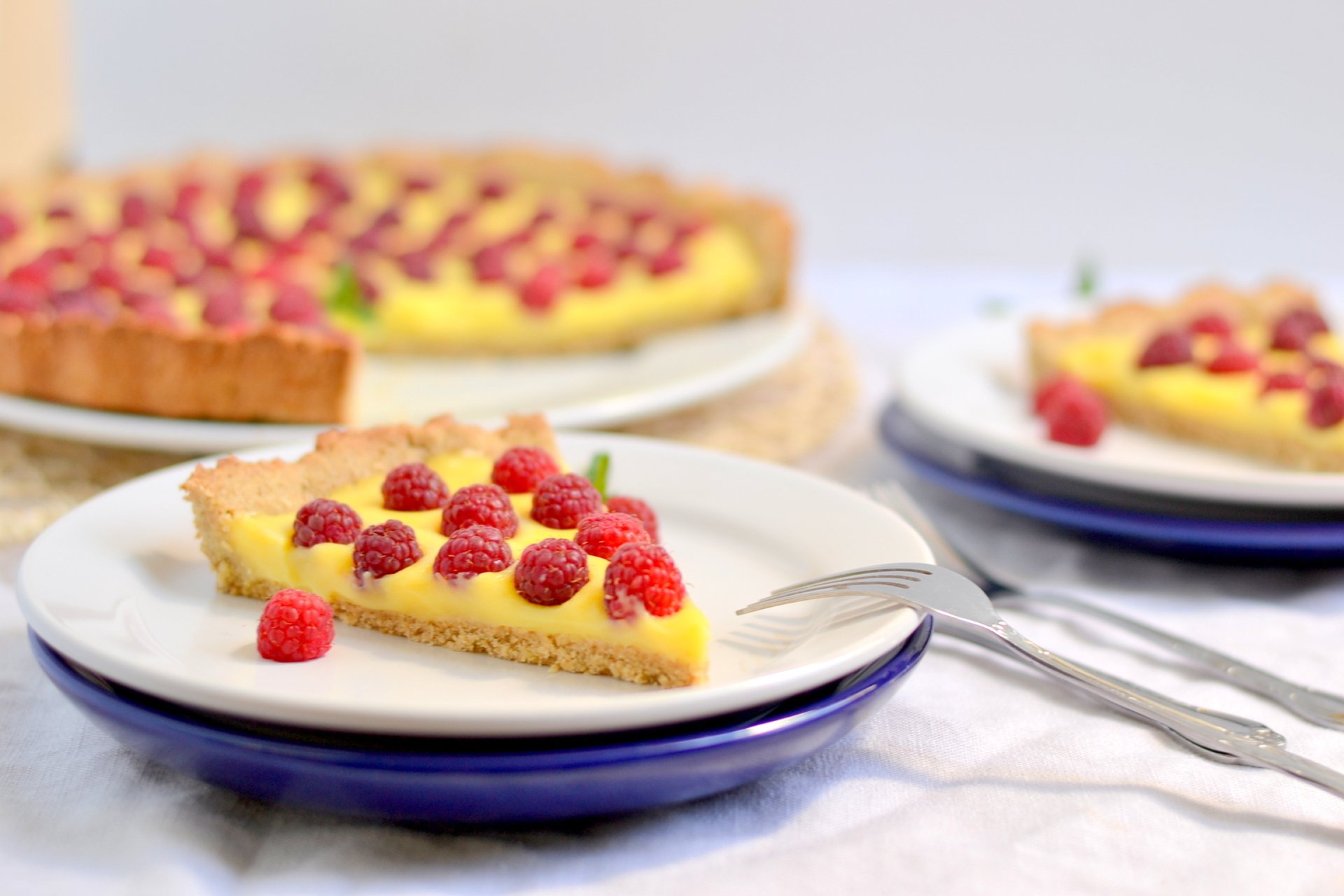 HD PC desktop wallpaper featuring a close-up of a slice of creamy pie topped with fresh raspberries on a white plate, with the whole pie blurred in the background.