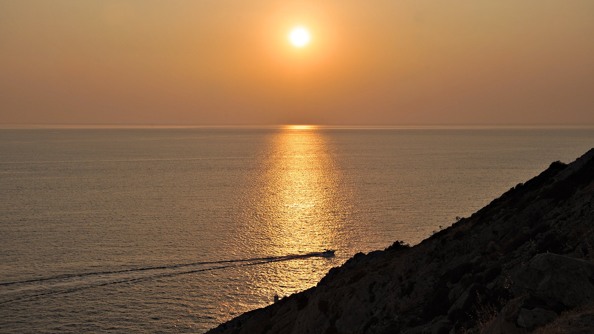 HD desktop wallpaper featuring a serene nature scene of a sunset over calm ocean waters, with a silhouetted hillside in the foreground.