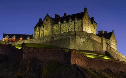 HD desktop wallpaper showcasing Edinburgh Castle illuminated against a deep blue twilight sky, highlighting its historic stone architecture and imposing presence.