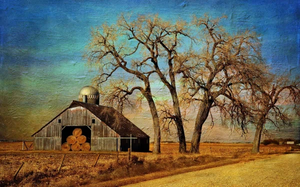 A picturesque farm scene featuring a rustic barn and bare trees under a vibrant sky, creating a serene backdrop for a desktop wallpaper.